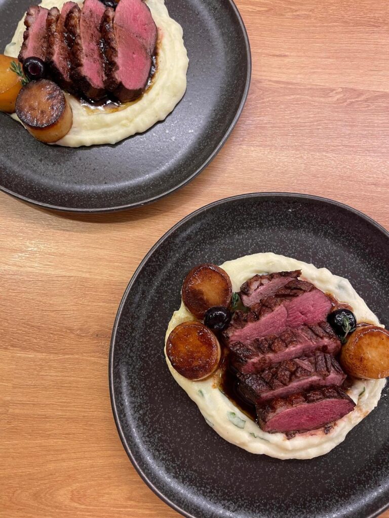 木製テーブルに並ぶ二皿の肉料理